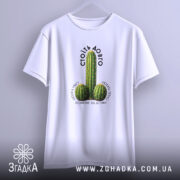 Футболка Стоїть довго, біла, підвішена на вішалці, з принтом кактусів, фон світло-сірий, текст над принтом чорний, напис 'СТОЇТЬ ДОВГО' розташований зверху.