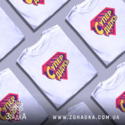 Футболка супер дідусь, біла, на моделі, з легким ракурсом спереду, фон пастельного кольору, принт у вигляді червоного герба з жовтим написом 'Супер дідусь'.