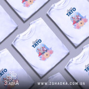 Футболка супер тато білого кольору, зображена на молодому чоловікові, фон світло-фіолетовий, принт містить малюнок батька і сина у супергеройських костюмах з квітами.