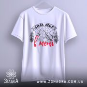 Футболка сила лісу в мені білого кольору, підвішена на вішалці, фон світлий, принт з горами та деревами в чорному кольорі з червоним написом, видно деталі крою.