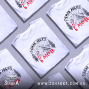 Футболка сила лісу в мені білого кольору, зображена на моделі, яка позує в три чверті, фон м'який пастельний, принт з горами та деревами в чорному кольорі з червоним написом.