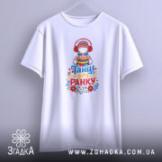 Футболка танці до ранку, біла, підвішена на вішалці, фон світло-сірий, принт з дівчиною в національному вбранні з навушниками, яскраві кольори принта, текст 'Танці до ранку' внизу.