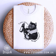 Футболка тяжко жити шкода вмерти, біла, складена на кошику, ракурс зверху, фон світло-сірий, принт з чорним котом у окулярах, що тримає пляшку та келих, текст навколо принта.