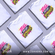 Футболка тобі пасує усмішка. Біла футболка на молодому чоловікові, зображена в анфас. Фон світло-фіолетовий, принт яскравий з написом 'Тобі пасує усмішка' в жовтому, чорному та рожевому кольорах, з кольоровими краплями.