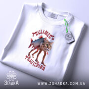 Футболка Trulimero Trulichina білого кольору, складена на поверхні, принт з котом і рибою, текст виконаний червоним кольором, на футболці є етикетка з зеленим шнурком.