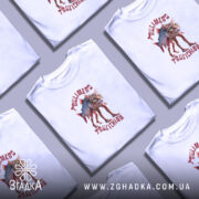 Футболка Trulimero Trulichina білого кольору, зображена на молодій людині, що позує на нейтральному фоні, принт зображує кота з риб'ячим тілом, текст на футболці виконаний червоним кольором.