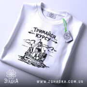 Футболка тримайся курсу, біла, лежить на плоскій поверхні, фон світло-сірий, принт з малюнком корабля та написом 'Тримайся курсу' у чорному кольорі, на комірці є етикетка.