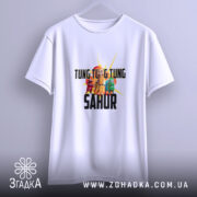 Футболка Tung Tung Sahur білого кольору, підвішена на вішалці, фон світло-сірий, принт з персонажами та текстом яскраво виділяється на тканині.
