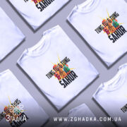 Футболка Tung Tung Sahur білого кольору, зображена на моделі в ракурсі спереду, фон світло-фіолетовий, принт з яскравими персонажами та текстом на чорному фоні.