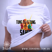 Футболка Tung Tung Sahur білого кольору, складена на поверхні, з видимим принтом, фон світло-сірий, на етикетці присутня зелена стрічка.