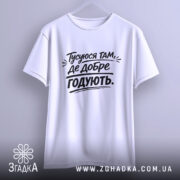 Футболка тусуюся, біла, підвішена на вішалці, фон світло-сірий, принт чорний з текстом 'Тусуюся там, де добре годують.'