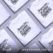 Футболка тусуюся, біла, зображена на чоловікові в ракурсі спереду, фон світло-фіолетовий, принт чорний з текстом 'Тусуюся там, де добре годують.'