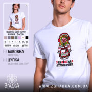 Футболка українська атмосфера, біла, на моделі, з принтом у вигляді ляльки-мотанки в традиційному вбранні, фон світло-фіолетовий, деталі принта яскраві, з червоними навушниками та кольоровим головним убором.