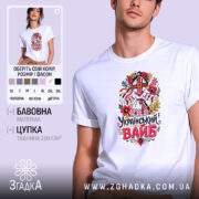 Футболка український вайб білого кольору, зображена на молодому чоловіку в анфас, фон світло-фіолетовий, принт з традиційним українським мотивом, що включає в себе квіти та ляльку-мотанку, текст "Український вайб" виконаний у яскравих кольорах.