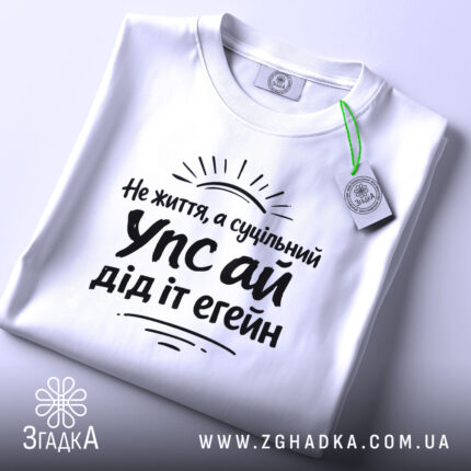 Футболка упс ай дід іт егейн, біла, на столі, з етикеткою, фон світло-сірий, принт чорного кольору з текстом і сонячними променями.