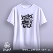 Футболка усміхнись якщо хочеш мене. Біла футболка, підвішена на вішалці, з принтом чорного кольору. Фон світло-сірий, футболка має класичний крій.