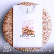 Футболка ведмедик і удача, біла, зображена на плоскій поверхні з плетеним декором, фон світлий, принт з ведмедиком у сонцезахисних окулярах та написами 'Lucky You' і 'Best of Luck'.