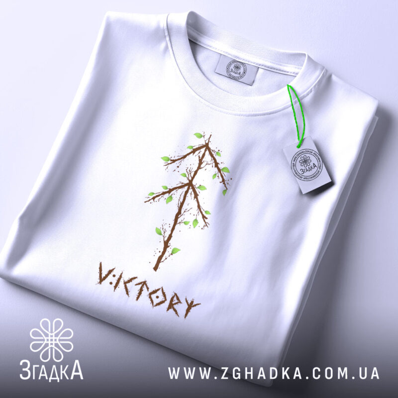 Футболка VIKTORY білого кольору, складена на поверхні, з видимим принтом у вигляді дерева з коричневими гілками та зеленим листям. На верхній частині футболки видно етикетку з логотипом, фон світло-сірий.