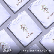 Футболка VIKTORY білого кольору, зображена на молодій людині, яка позує в три чверті, фон світло-фіолетовий. Принт у вигляді дерева з коричневими гілками та зеленим листям, розташований по центру, під ним напис 'VIKTORY' коричневого кольору.