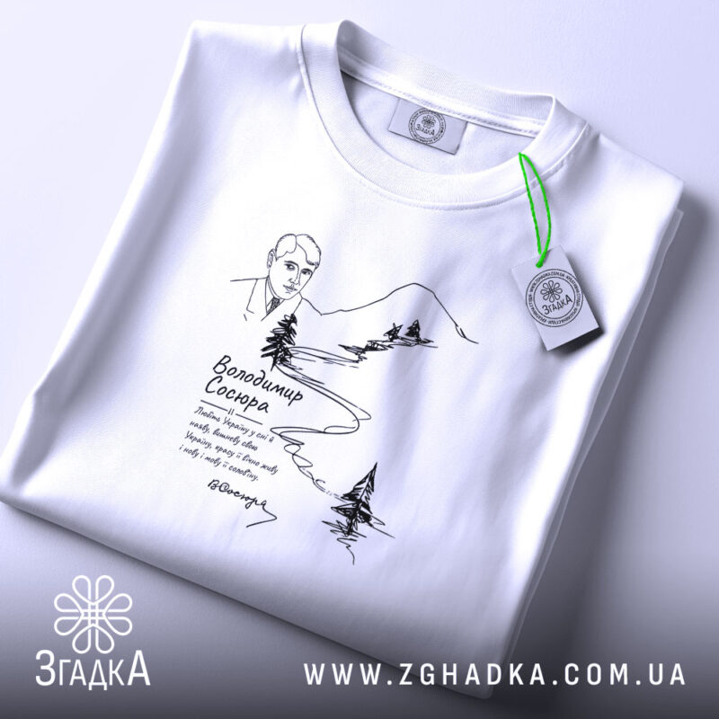 Футболка Володимир Сосюра з автографом, біла, складена на поверхні, з верхнього ракурсу, фон світлий, принт з малюнком автора та пейзажем, прикріплений етикет.
