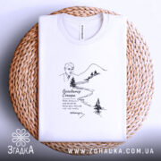 Футболка Володимир Сосюра з автографом, біла, складена на плетеній кошику, фон світлий, принт з малюнком автора та пейзажем, текст під малюнком.