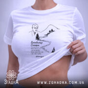 Футболка Володимир Сосюра з автографом, біла, складена на поверхні, з верхнього ракурсу, фон світлий, принт з малюнком автора та пейзажем, прикріплений етикет.