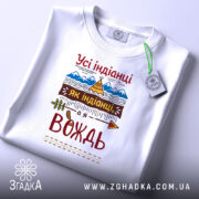 Футболка вождь племені, біла, складена на поверхні, фон світло-сірий, принт з текстом "Усі індіанці як індіанці, а я вождь" та графічними елементами, такими як гори та намет.