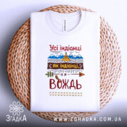 Футболка вождь племені, біла, складена на плетеній кошику, фон світло-сірий, принт з текстом "Усі індіанці як індіанці, а я вождь" та малюнками гір і намету.