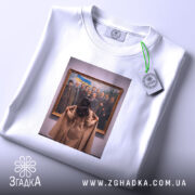 Футболка видатні українці, біла, на плоскій поверхні, з принтом, що зображує жінку, яка дивиться на групу чоловіків у картині, фон світло-сірий, деталі принта чіткі, зображення в золотій рамі, етикетка з зеленим шнурком.