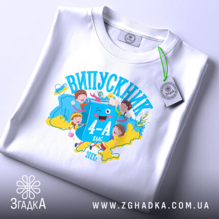 Футболка випускник молодшої школи, білого кольору, розкладена на поверхні. На фоні ніжно-фіолетовий колір. Принт яскравий, з малюнками дітей, книжок та написом 'ВИПУСКНИК 4-А клас', виконаний у синіх та жовтих тонах.