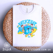 Футболка випускник молодшої школи, білого кольору, розкладена на плетеній кошику. На фоні ніжно-фіолетовий колір. Принт яскравий, з малюнками дітей, книжок та написом 'ВИПУСКНИК 4-А клас', виконаний у синіх та жовтих відтінках.