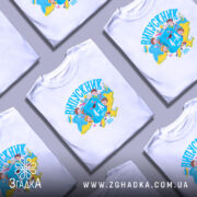 Футболка випускник молодшої школи, білого кольору, зображена на молодій людині, яка позує в три чверті. На фоні ніжно-фіолетовий колір. Принт містить яскраві кольори: синій, жовтий та червоний, з малюнками дітей та книжок, а також написом 'ВИПУСКНИК 4-А клас'.