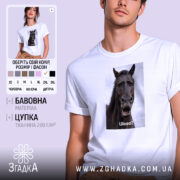 Футболка з мемним конем, білого кольору, зображена на молодій людині, яка дивиться в камеру. Принт з конем займає центральну частину, на ньому написано 'Шо?' у нижній частині. Фон світло-фіолетовий, що підкреслює яскравість футболки.