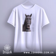 Футболка з мемним конем, білого кольору, підвішена на вішалці. Принт з конем займає центральну частину, на ньому написано 'Шо?'. Фон світло-сірий, що підкреслює простоту дизайну футболки.