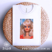 Футболка з мемним обличчям барбі, біла, на круглому кошику, фон світло-фіолетовий, принт зображує барбі з великими блакитними очима та світлим волоссям, одягнена в червону сукню.