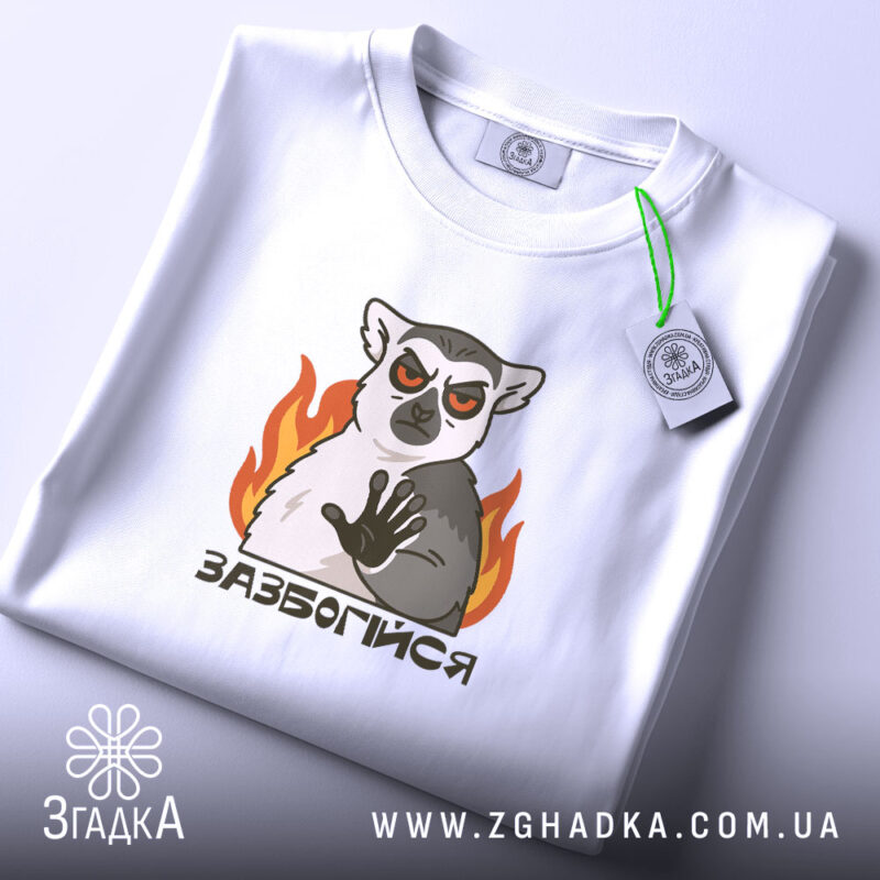 Футболка зазбогійся з лемуром, біла, знята зверху, фон світло-сірий, принт з лемуром з червоними очима та вогнем, етикетка на рукаві.