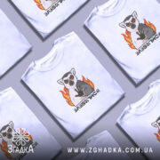 Футболка зазбогійся з лемуром, біла, на моделі з легким ракурсом, фон світло-фіолетовий, принт з лемуром з червоними очима та вогнем.