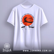 Футболка журавлі та мрія, біла футболка, зображена на вішалці, ракурс спереду, фон світло-сірий, принт з червоним сонцем та журавлями, текст на футболці українською мовою.