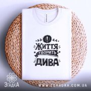 Футболка життя творить дива, складена, біла, на плетеному фоні, бренд Згадка.
