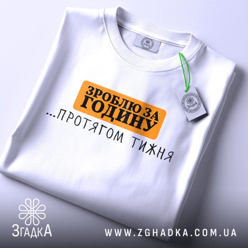 Футболка зроблю за годину. Біла футболка, складена на столі, з принтом чорного та оранжевого кольорів. Напис 'ЗРОБЛЮ ЗА ГОДИНУ ...ПРОТЯГОМ ТИЖНЯ' розташований по центру. Фон світлий, з легким відблиском.