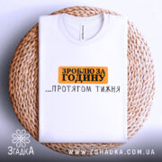 Футболка зроблю за годину. Біла футболка, складена на плетеному кошику, з принтом чорного та оранжевого кольорів. Напис 'ЗРОБЛЮ ЗА ГОДИНУ ...ПРОТЯГОМ ТИЖНЯ' розташований по центру. Фон світлий, з натуральними текстурами.