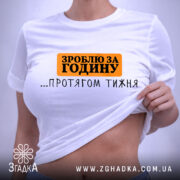 Футболка зроблю за годину. Біла футболка, складена на столі, з принтом чорного та оранжевого кольорів. Напис 'ЗРОБЛЮ ЗА ГОДИНУ ...ПРОТЯГОМ ТИЖНЯ' розташований по центру. Фон світлий, з легким відблиском.
