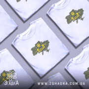 Футболка ЗСУ стиль, біла футболка на моделі, з принтом у вигляді карти України з камуфляжним малюнком, жовтий герб тризуба та напис 'Severe and Zealous', фон світло-фіолетовий, модель з легким макіяжем і розпущеним волоссям.