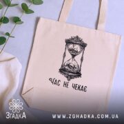 Шопер час не чекає символ життя, бежевий шопер на столі, зелена рослина.