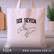 Шопер six seven жест руками, бежевий, на столі, з рослиною на фоні,.