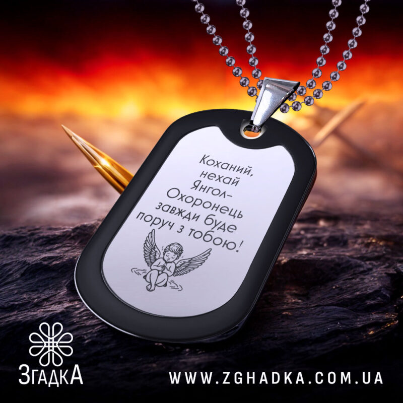 Жетон янгол охоронець чорного кольору з матовою поверхнею, зображення з ракурсу спереду на фоні з червоними та жовтими відтінками, видно кулю на задньому плані.