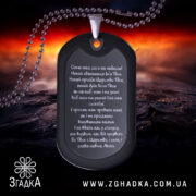 Жетон Отче наш, чорного кольору, матова поверхня, зображений з верхнього ракурсу на фоні з червоними та чорними відтінками, видно текст молитви на жетоні та металевий ланцюжок.