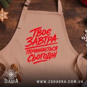 Фартух твоє завтра починається сьогодні, бежевий на дерев'яному фоні, бренд Згадка.