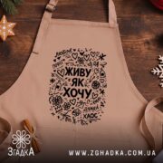 Фартух живу як хочу, бежевий, на дерев'яному фоні, бренд Згадка.