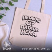 Шопер питання є питань нема, бежевий колір, на столі з рослинами, бренд.